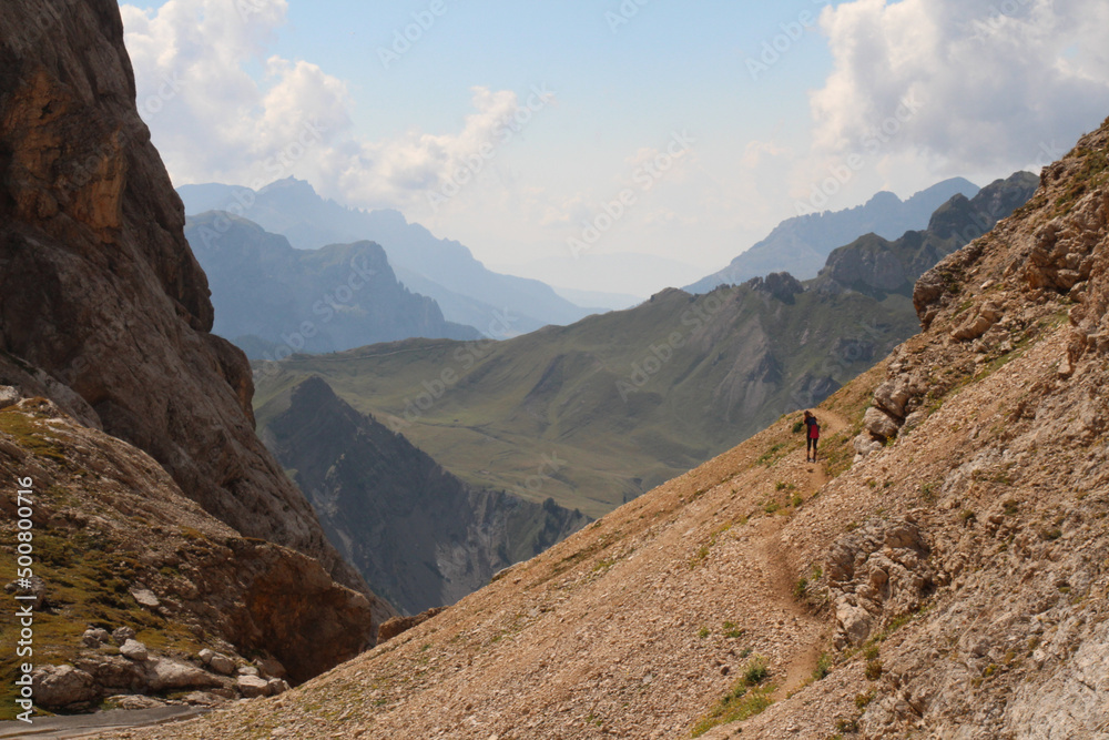 Mountain landscape with a tourist on a hiking trail at Passo Ombretta in a sunny day, Italian Alps.