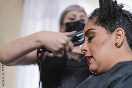 Latina woman in beauty salon while hairdresser irons her hair