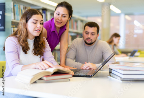Group of people looking at laptop screen together in library and preparing for exam