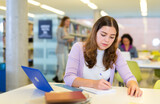 Adult female student with laptop and books in public library