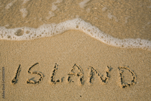 Island - handwritten on the soft beach sand.