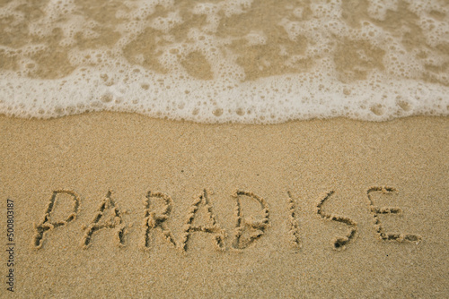 Paradise - handwritten on the soft beach sand.
