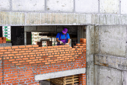 Construction of a brick wall in a monolithic frame building, a bricklayer lays out a partition along a thread photo