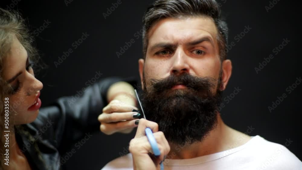 Cutting long beard. Young beautiful couple of beautiful fashionable female barber cutting beard and holding scissors and handsome man with long beard. Beard shaving.