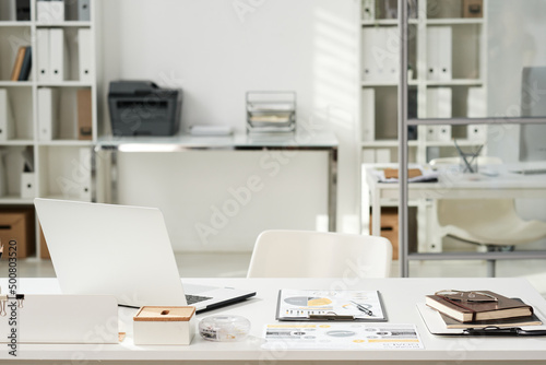 Office interior with white table with open laptop, financial documents and organizer and chair