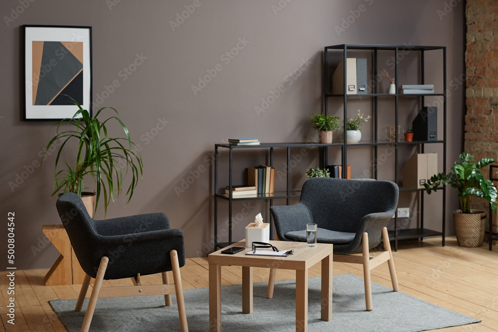 Fototapeta premium Horizontal no people shot of modern psychologist office interior in gray and brown colors with two chairs and coffee table