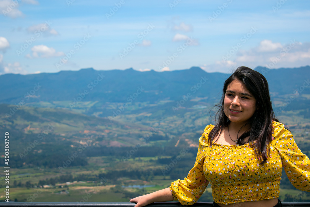 mujer sonriente con camiseta color amarilla sonteniendo un barandal en un dia soleado 