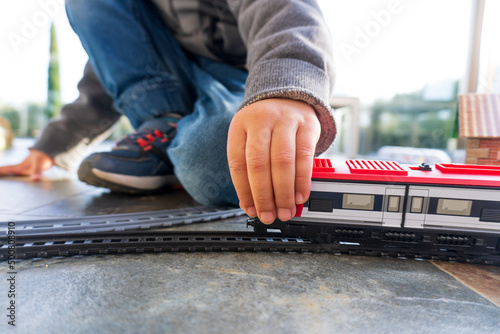 Niño jugando Young kid playing with toy trains on the floor. Toy train similar to Cercanias Renfe Spanish train and Ave high speed traincon trenes