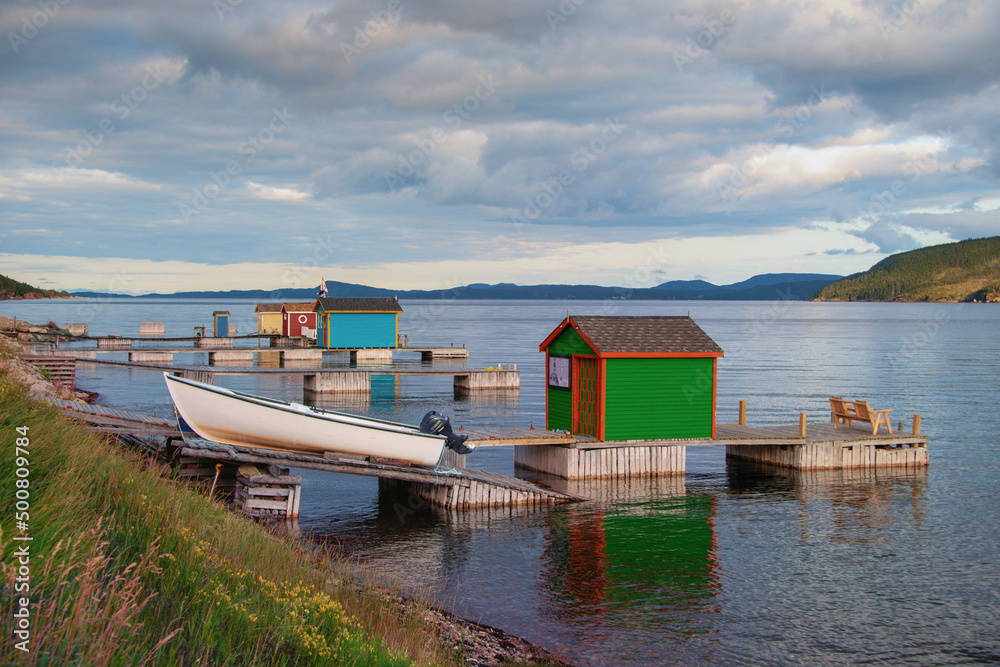 Burlington, Newfoundland, Canada-May 2022: A small fishing community, with small white fishing boats on a wooden slipway in the harbour with vintage colorful wooden buildings along the shoreline. 