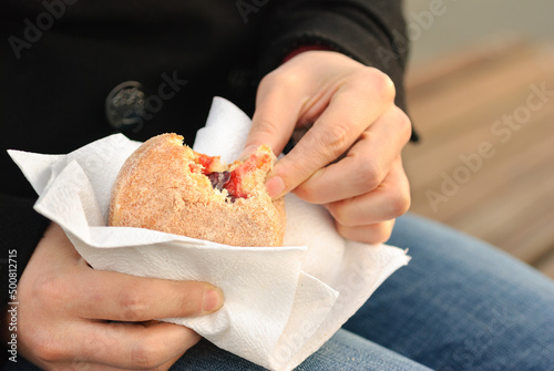 Woman sitting on a bench eating a jelly donut on a fall day.