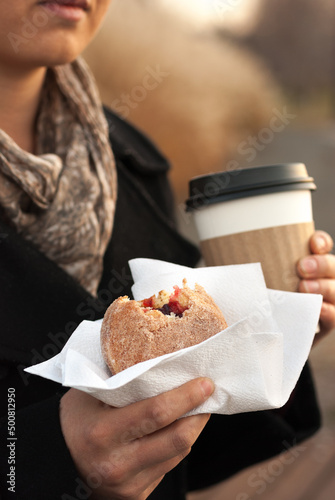 A Woman Holding a Jelly Donut and a Coffee on a Fall Day.