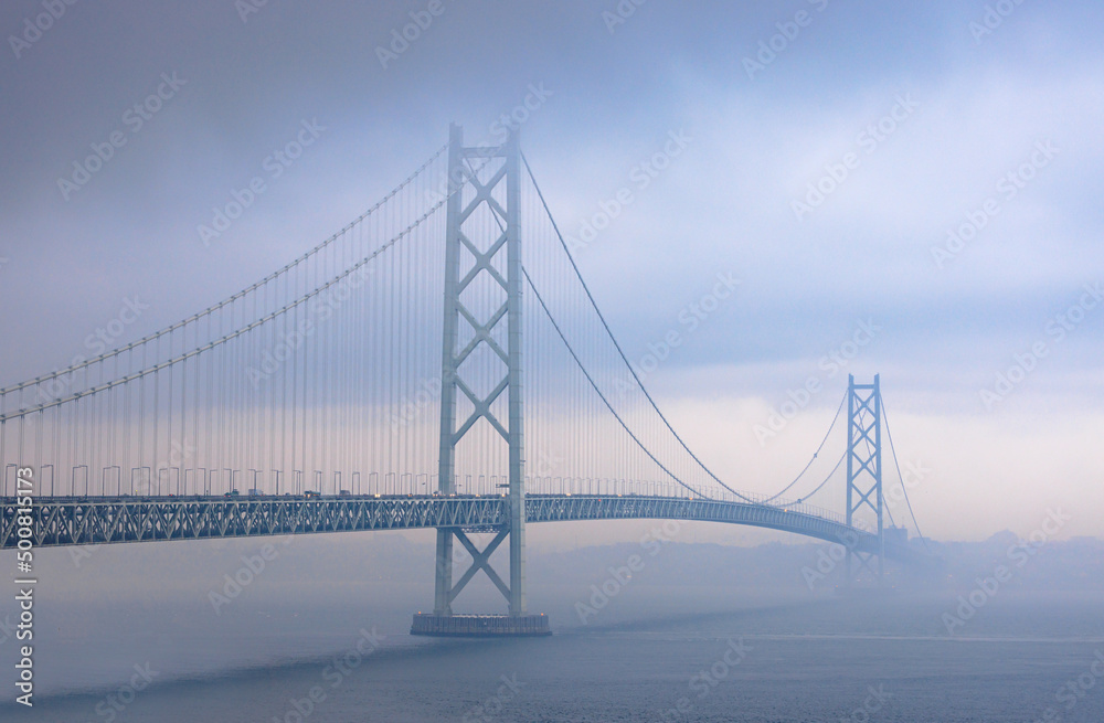 Suspension bridge in dark clouds and fog with hint of sunset Suspension bridge in dark clouds and fog with hint of sunset
