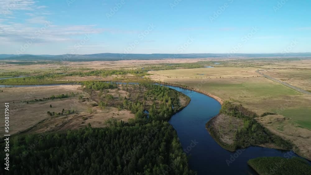 Aerial view of a river flowing through rural area with meadows, rare trees and with the road on the distance Aerial view of a river flowing through rural area with meadows, rare trees and with the road on the distance
