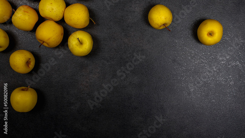 Yellow sweet ripe apples are scattered on the black table