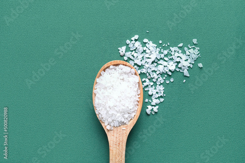 Wooden spoon with sea salt on green background photo