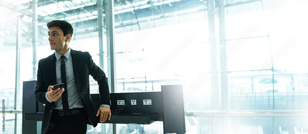 Portrait of young Elegant businessman using mobile phone app check-in boarding pass in airport.Handsome business professional man wearing suit texting smartphone inside office building or terminal  - obrazy, fototapety, plakaty 