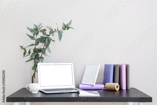 Workplace with laptop, plant branches in vase and cup near light wall