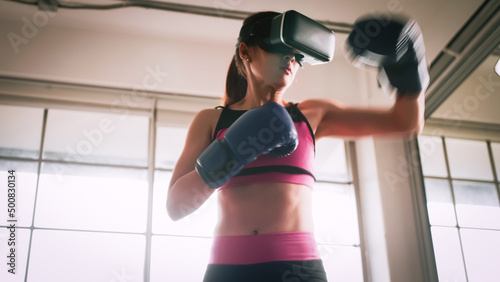 Young Asian woman wearing virtual reality glasses while working out at home. © ronnarong