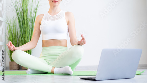 Yoga online. Home meditation. Sporty hobby. Unrecognizable fit woman in sportswear doing lotus pose exercise on fitness mat at laptop relax video course indoors.