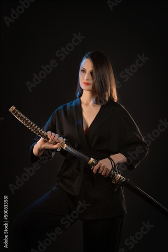 A young beautiful woman in a black kimono draws a Japanese saber from its scabbard