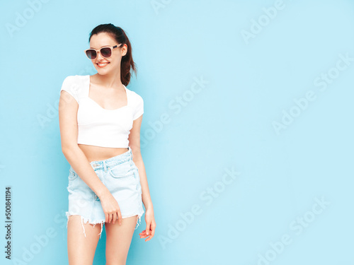 Young beautiful smiling female in trendy summer jeans skirt and top clothes. Sexy carefree woman posing near blue wall in studio. Positive brunette model having fun.Cheerful and happy