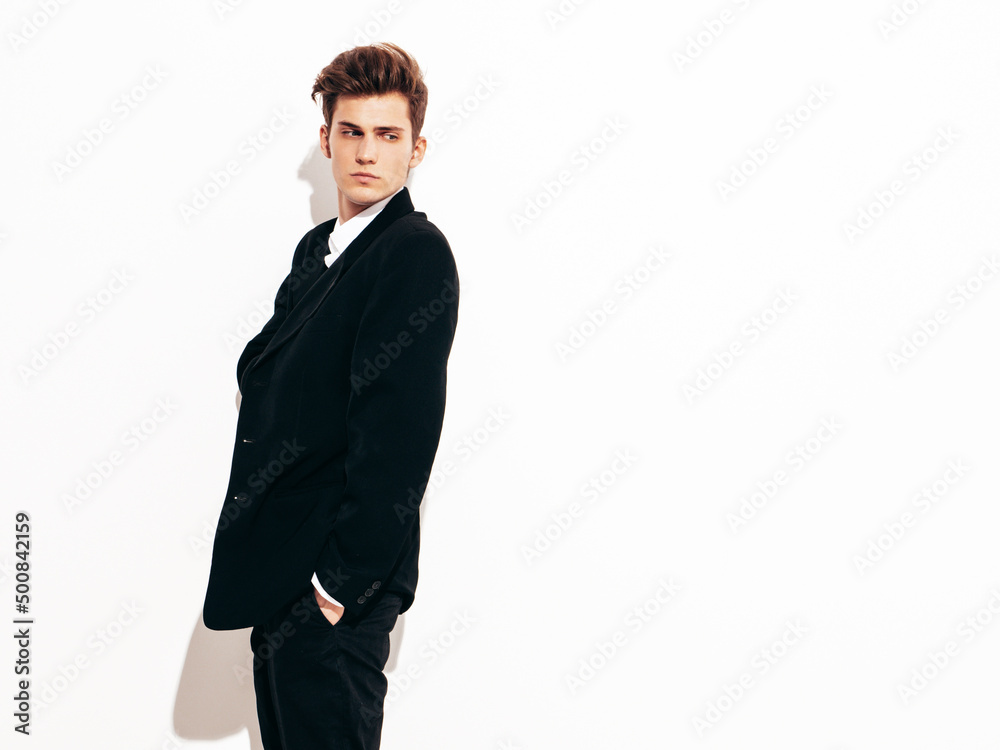 Portrait of handsome confident stylish hipster lambersexual model. Sexy modern man dressed in elegant black suit. Fashion male posing in studio near white wall. Isolated Portrait of handsome confident stylish hipster lambersexual model. Sexy modern man dressed in elegant black suit. Fashion male posing in studio near white wall. Isolated
