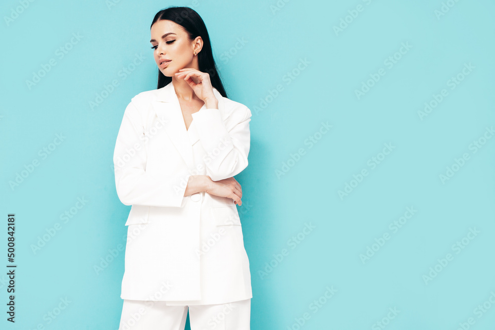High fashion portrait of young beautiful brunette woman wearing nice trendy white suit. Sexy fashion model posing in studio. Fashionable female isolated on blue High fashion portrait of young beautiful brunette woman wearing nice trendy white suit. Sexy fashion model posing in studio. Fashionable female isolated on blue