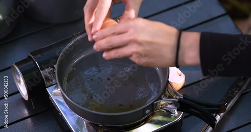 Close up shot, Selective focus, Female hands put an egg into hot oil in pan, cooking easy meal in nature park