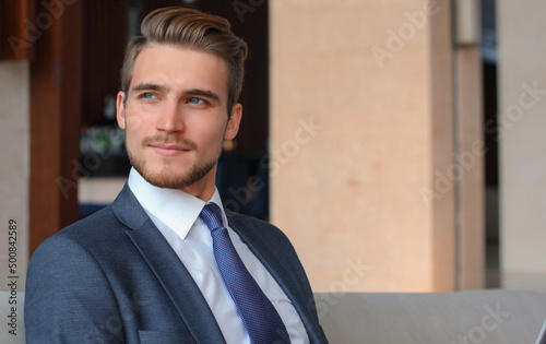 Young businessman working on laptop, sitting in hotel lobby waiting for someone