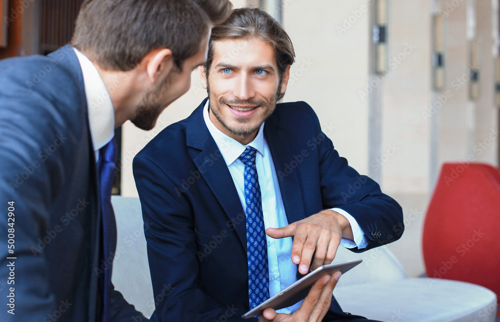 Two young businessmen using touchpad at meeting. Two young businessmen using touchpad at meeting.
