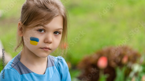 Portrait of a sad girl 8 years old with a Ukrainian flag on her face