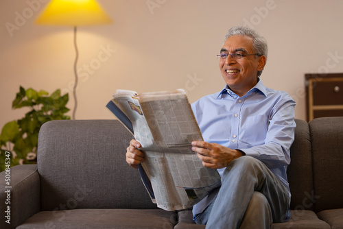 Senior man reading newspaper while sitting on sofa at home