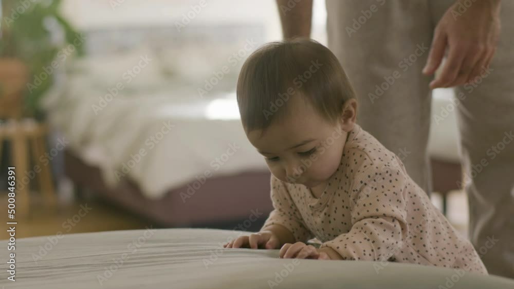 Cute little baby in pajamas playing in parents bed on weekend morning. Baby girl trying getting on sofa while her dad looking after her. Family, children concept Cute little baby in pajamas playing in parents bed on weekend morning. Baby girl trying getting on sofa while her dad looking after her. Family, children concept