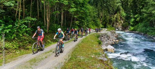 Canvas Viele Mountainbiker radeln an einem Wildbach in den Alpen entlang aufwärts