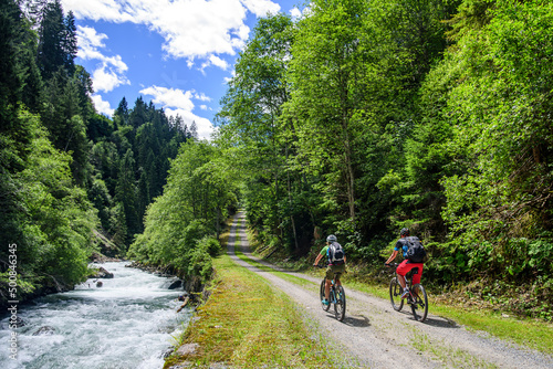 Zwei Mountainbiker radeln an einem Wildbach in den Alpen entlang aufwärts
