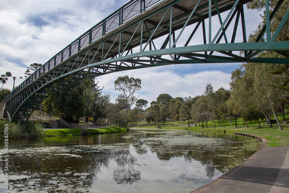 Bridge over the river in the city park surrounded by green trees, cityscape