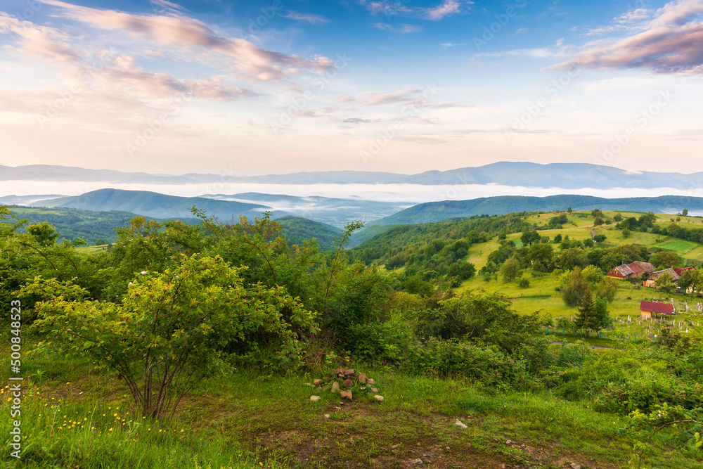 carpathian rural landscape in spring at sunrise. trees on the grassy hills rolling in to the distant valley in morning light. fluffy cloud formations on the sky. beautiful nature background