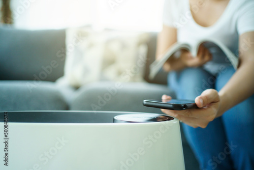 Woman control a modern air purifier through the application on a smartphone.