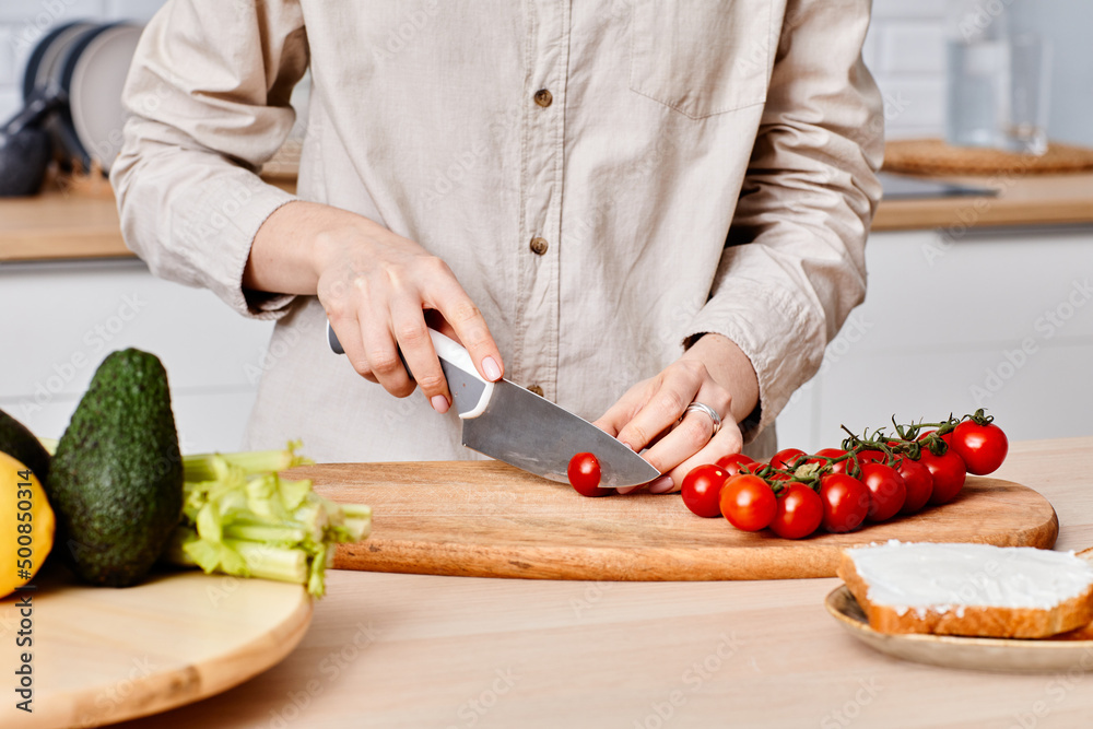 Close-up of young woman cutting cherry tomatoes with knife on cutting board at kitchen table Close-up of young woman cutting cherry tomatoes with knife on cutting board at kitchen table