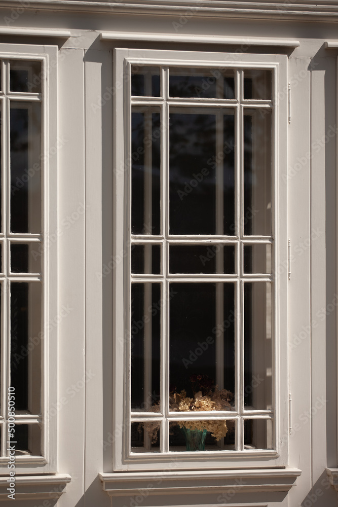 An old double window with a bouquet of dried flowers. A bouquet of dried flowers is between the two windows, in the sun. The window is white. There is a nostalgic atmosphere.