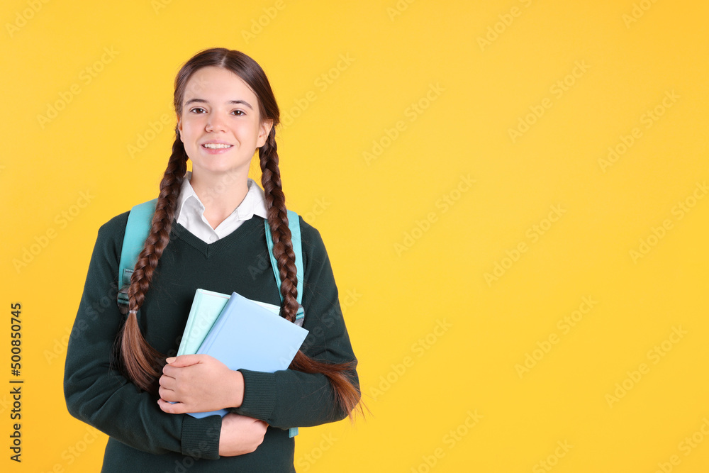 Teenage girl in school uniform with books and backpack on yellow background. Space for text Teenage girl in school uniform with books and backpack on yellow background. Space for text