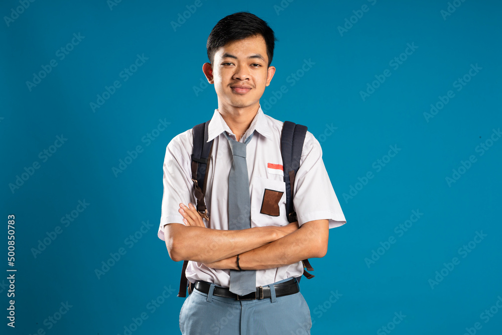 Back to school. Portrait of Indonesian high school student smiling at camera while crossing his arms isolated on blue background. Back to school. Portrait of Indonesian high school student smiling at camera while crossing his arms isolated on blue background.