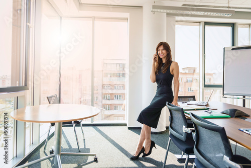 Confident businesswoman talking with somebody on mobile phone while standing at the office