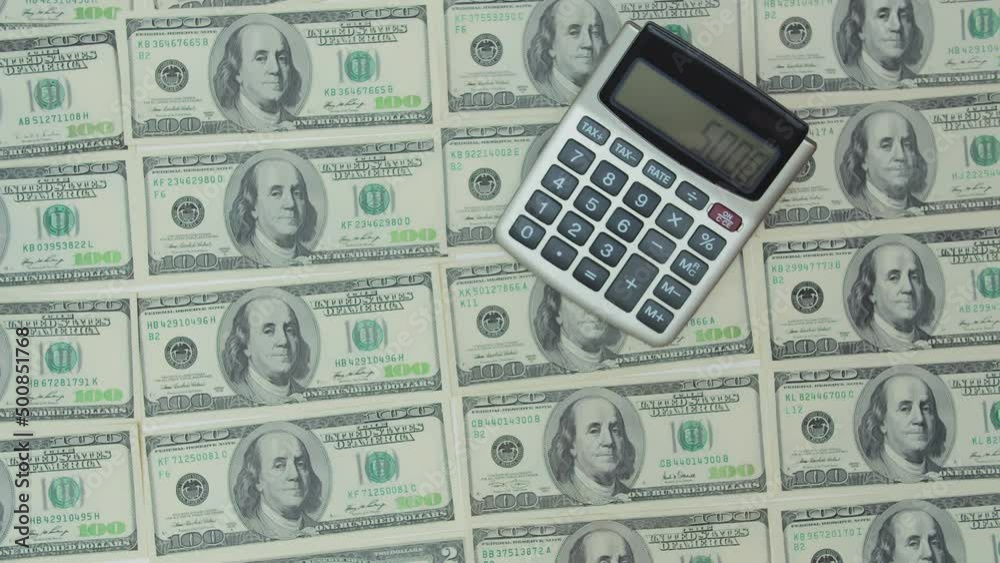 The calculator lies on flat layers of dollars. The human hand enters the value of five thousand on it. Benjamin Franklin's drawing on the banknotes The calculator lies on flat layers of dollars. The human hand enters the value of five thousand on it. Benjamin Franklin's drawing on the banknotes