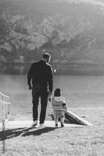 Un papa et son fils de dos face à lac, ils se baladent sur la berge