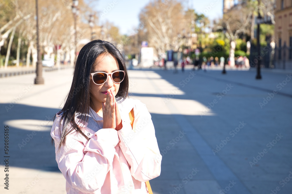 Young beautiful South American woman in a pink jacket and sunglasses, palms together praying. Concept religion, prayer, catholic, faith. Young beautiful South American woman in a pink jacket and sunglasses, palms together praying. Concept religion, prayer, catholic, faith.