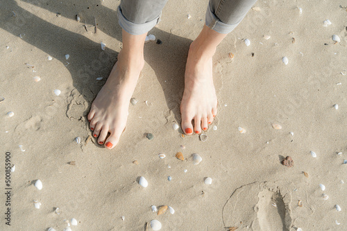 Woman standing barefeet on sand with seashells at beach photo