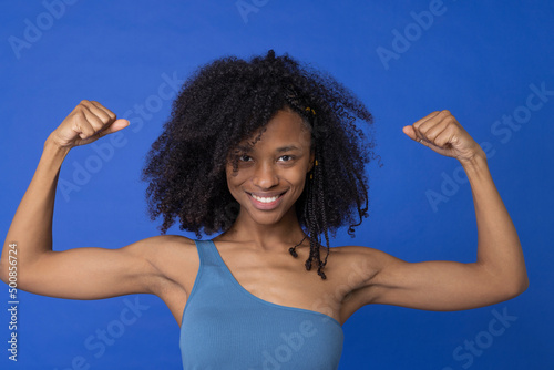 Smiling woman flexing muscles against blue background