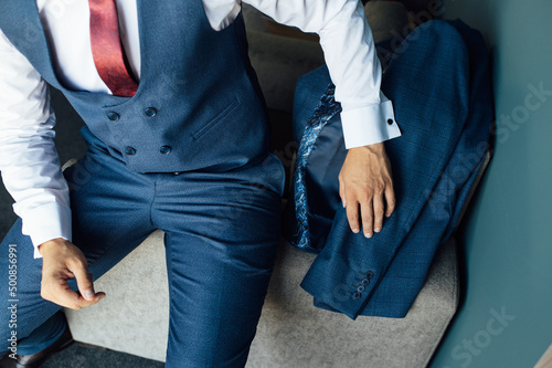 A young businessman in a blue suit takes the suit in his hand and puts it on