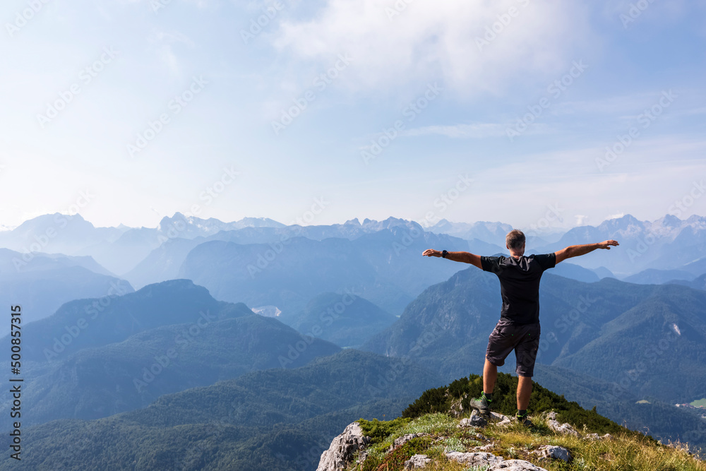 Man standing with arms outstretched on mountain peak on a sunny day Man standing with arms outstretched on mountain peak on a sunny day